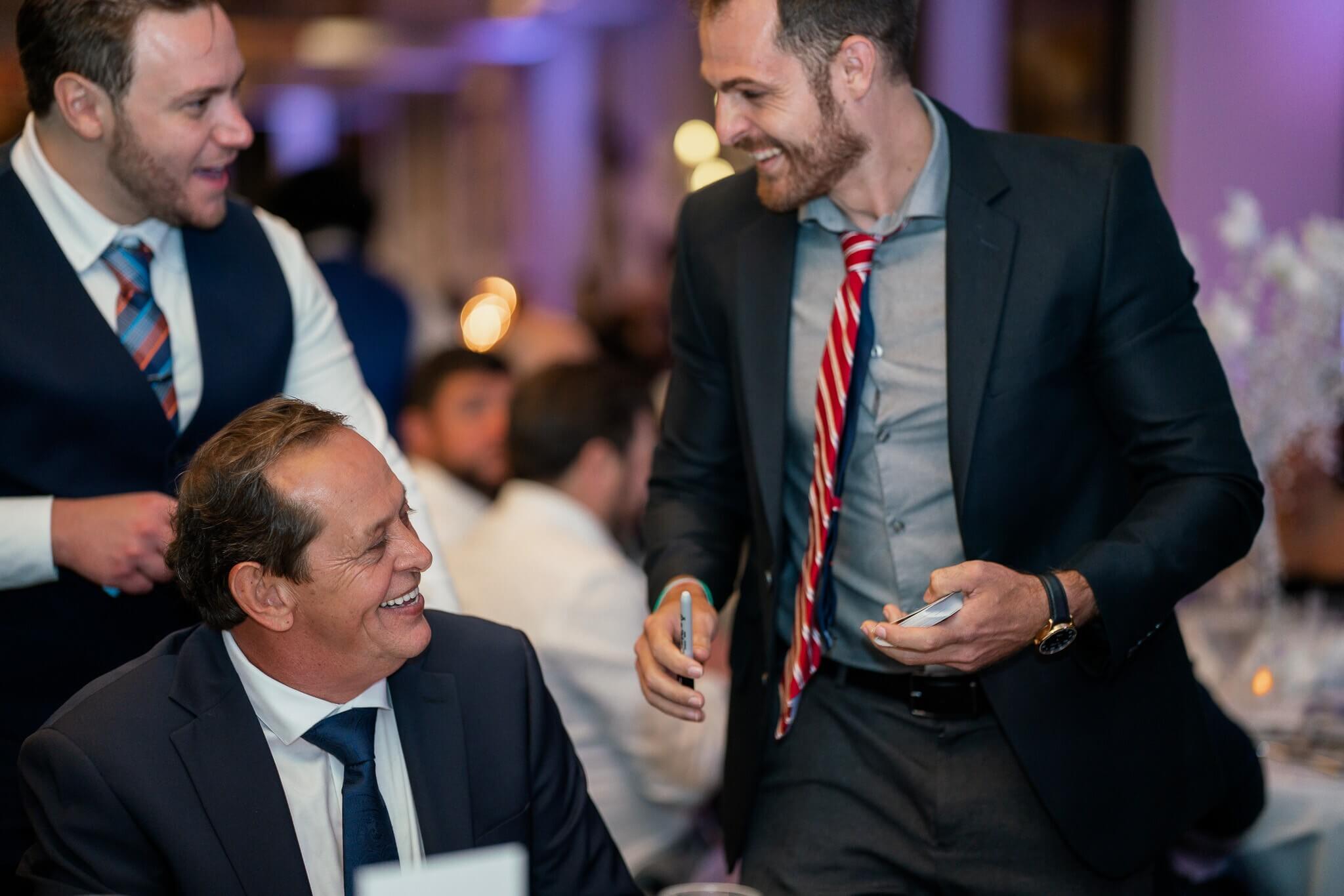 Corporate magician performing close-up card magic for laughing guests at a company event